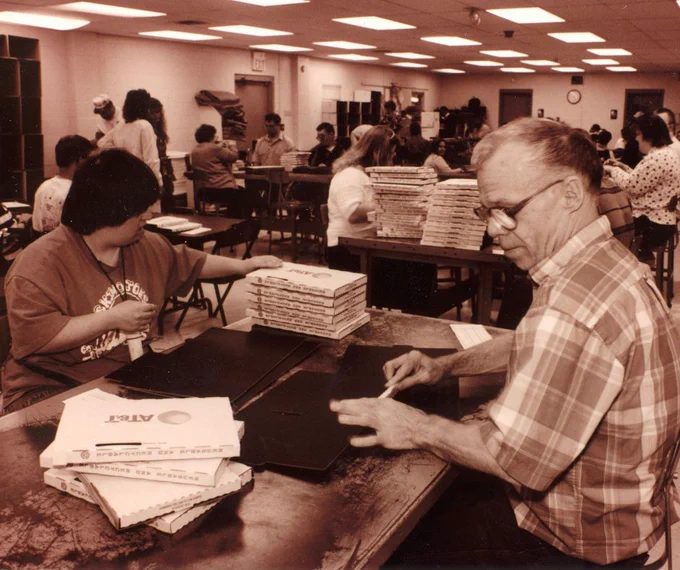 People in a workroom sitting down assembling small boxes with AT&T logo.