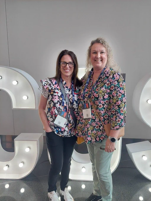 Two women in front of a large light display spelling out "CS". 