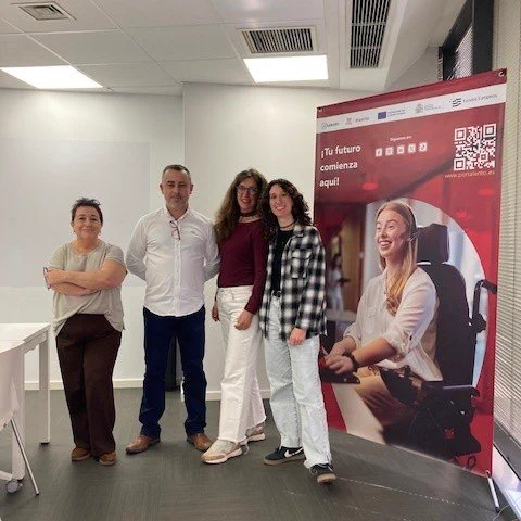 Foto de familia con cuatro personas de pie en una sala junto a un roll-up rojo de Inserta Empleo con el texto “Tu futuro comienza aquí” y un código QR. A la izquierda, mesas blancas y, al fondo, una pared con salidas de ventilación en el techo.
