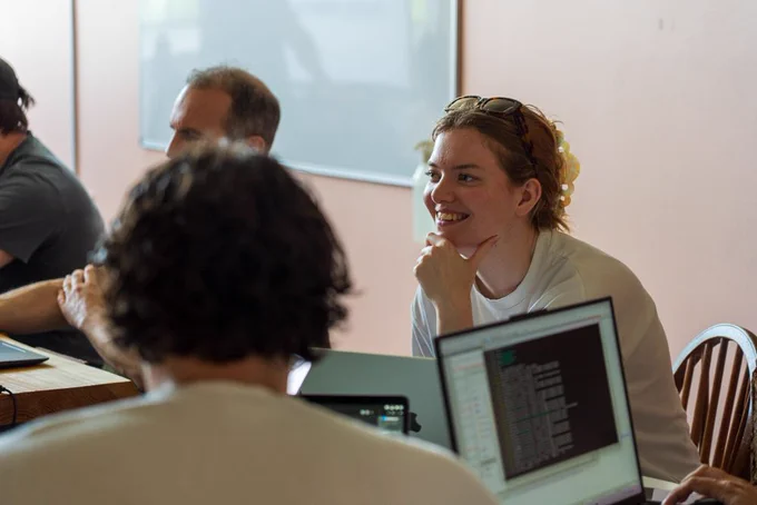 A woman smiling and listening attentively during a collaborative tech workshop session behind an open laptop.