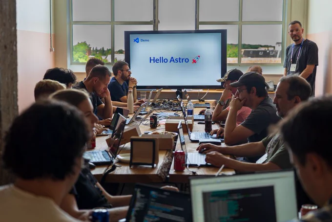 A room of developers with laptops sitting along a long table facing a presentation screen that reads "Hello Astro."