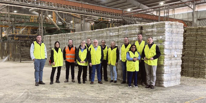 The AgriFutures Australia Board wearing yellow safety vests standing inside a large industrial warehouse with stacked bales of export fodder in the background.