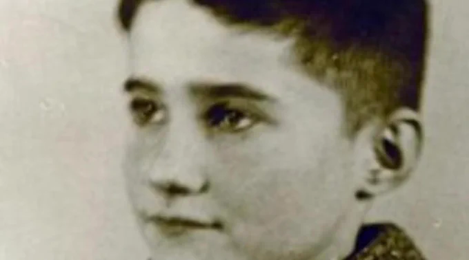 Historical black and white photo of a boy, featuring a close-up side profile. He has short hair. His expression is thoughtful.
