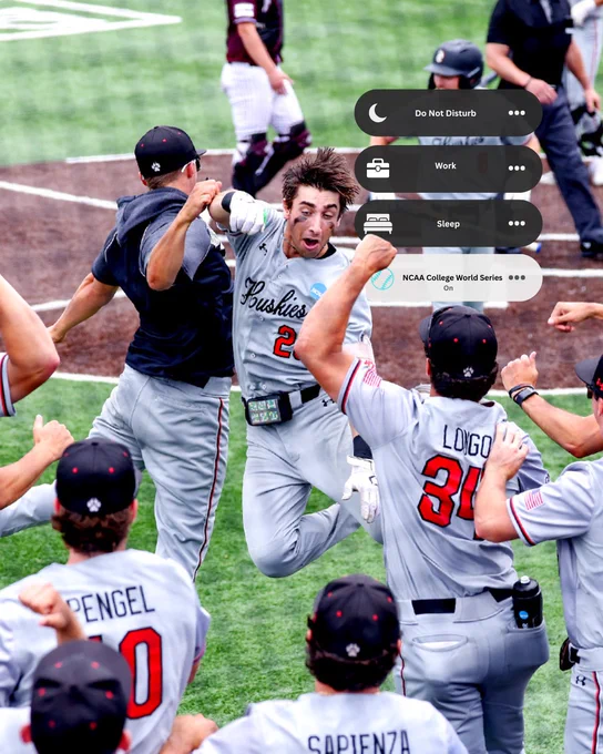 Baseball player in \"Huskies\" jersey #2 jumps excitedly, cheered by teammates.