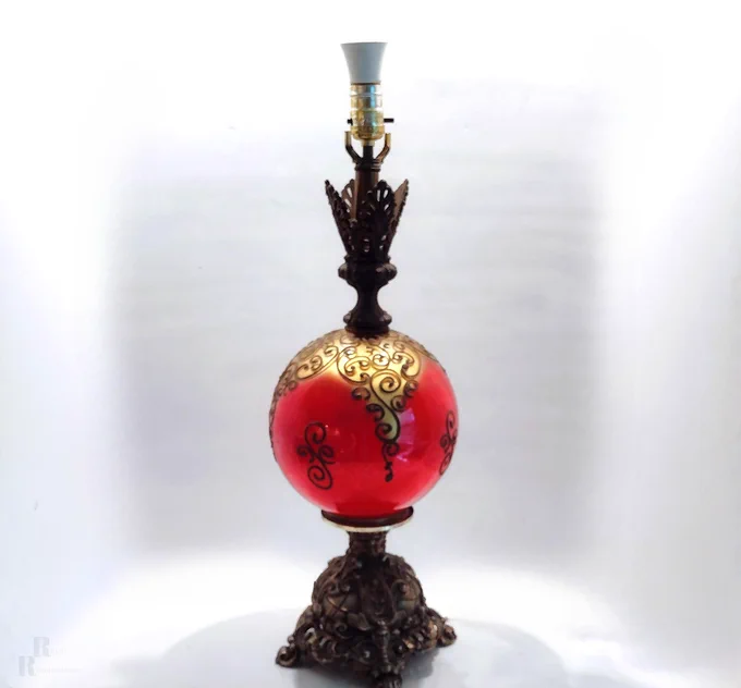 Mid‑century Falkenstein‑style lamp with an 8‑inch red‑and‑gold eglomisé glass globe, metallic paste relief gold scrollwork, and an ornate cast‑metal Rococo base; visible age wear on the globe and tarnish on the metal.