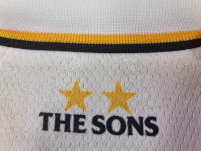 Close-up of a sports jersey featuring 'The Sons' text and two stars. The jersey has horizontal yellow and black stripes against a white background.