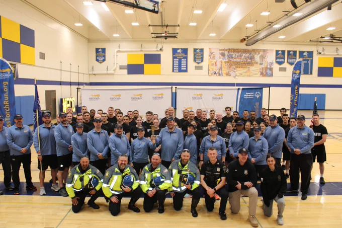 Large group of participants for the Special Olympics Massachusetts Torch Run posing in a gymnasium with banners and a Special Olympics backdrop.