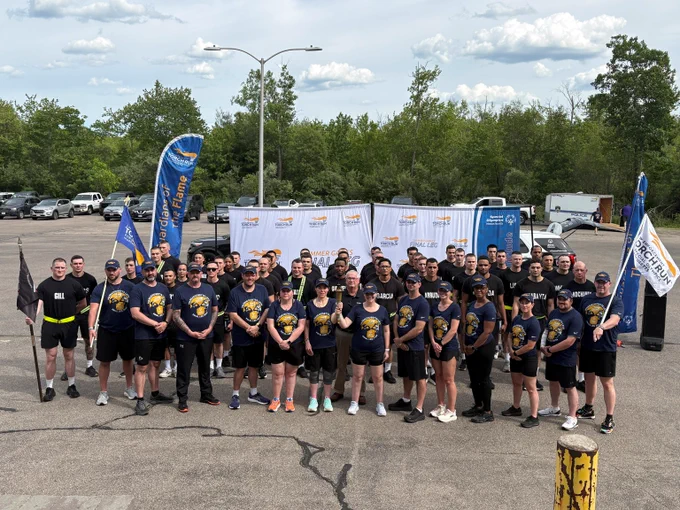 Large group of participants for the Special Olympics Massachusetts Torch Run posing in a outside with banners and a Special Olympics backdrop.