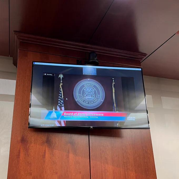 A monitor shows a livestream of a Board of State Canvassers meeting.