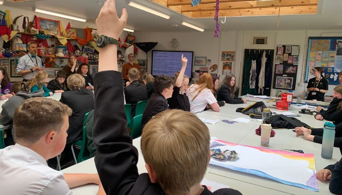 Students in a classroom actively participating, with several raising their hands to answer questions during a lesson.