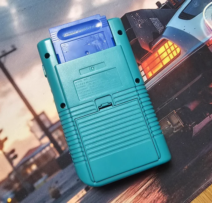 Ein Nintendo Game Boy in türkis von hinten. Ein blauer Cartridge steckt halb im Slot. 