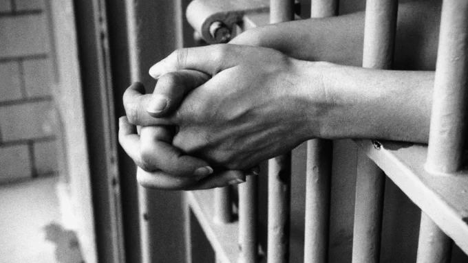 A woman's hands through prison bars.