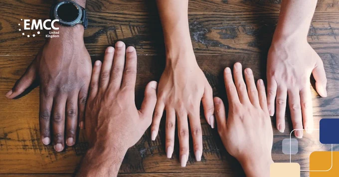 Four diverse hands placed side by side on a wooden table, symbolizing unity and collaboration.
