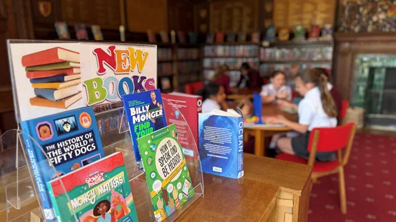 Display of children's books on a wooden stand in a library with children reading in the background.