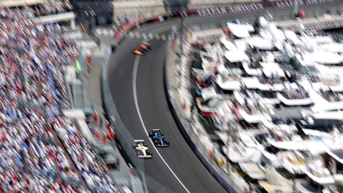 High-speed Formula 1 action at Monaco, cars blurred at pace along the harbour section with packed grandstands and yachts lining the circuit