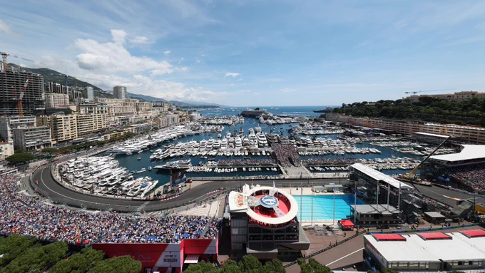 Monaco Grand Prix harbour view, Formula 1 street circuit wrapping around Port Hercules, yachts, grandstands, and the iconic start of the pit straight under clear skies