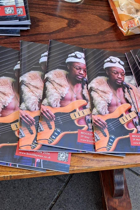 Stack of Brockley Max event booklets featuring a musician playing an electric bass guitar wearing a fur coat and sunglasses.
