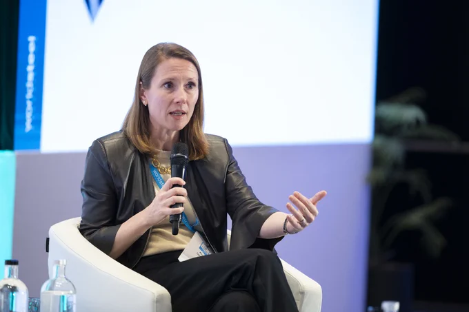 A woman sits in a chair and speaks into a microphone during a panel discussion.