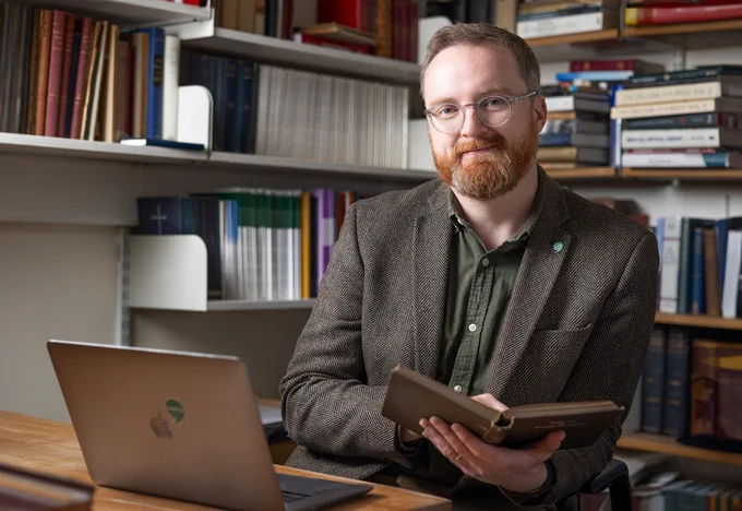 Colour head and shoulders photo of Dr James Eglinton sat at his desk whilst smiling at the camera