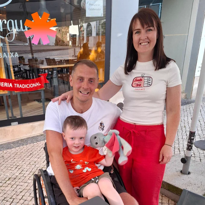 Photo of Samantha, her partner and her son smiling at the camera outside a cafe.