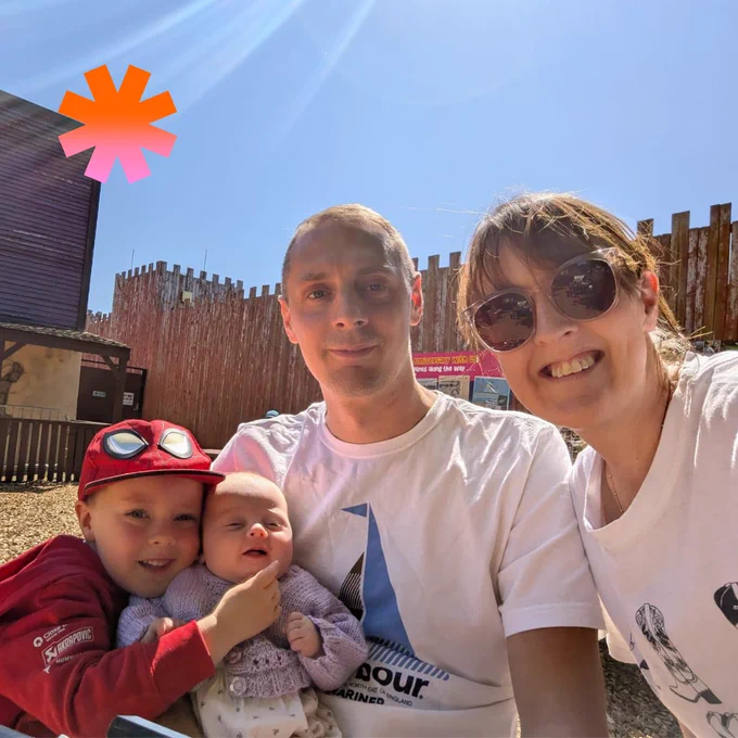 Selfie of Samantha, her partner and their two children smiling at the camera in a children's sand pit.