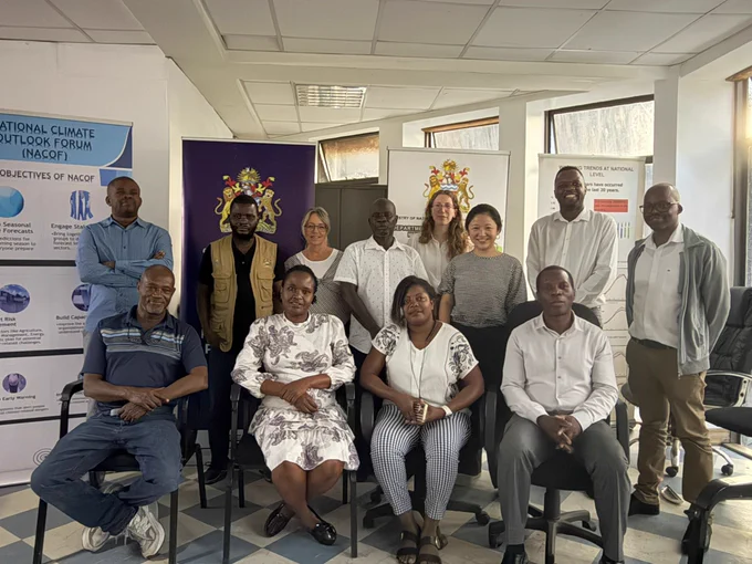 A group of people is gathered in an office setting, posing for a photo. There are banners visible in the background, including one labeled "IGAD Climate Prediction and Applications Centre (ICPAC)" and another featuring the Republic of Kenya's coat of arms. The group consists of individuals sitting and standing, all looking towards the camera.
