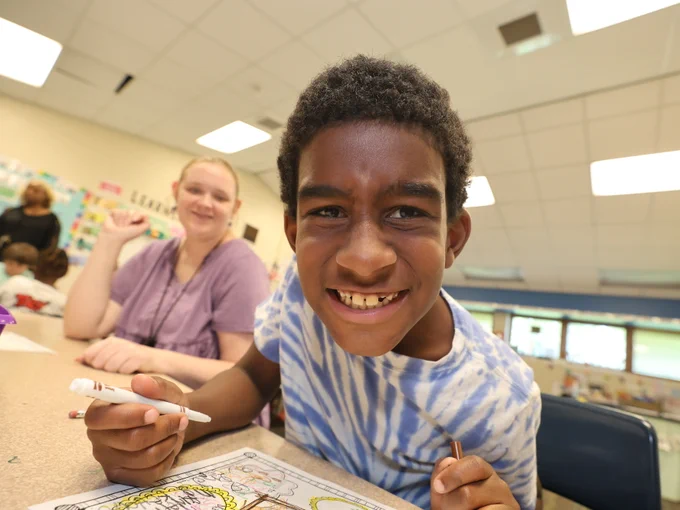 Summer learning student smiles at camera while working on a creative writing project.