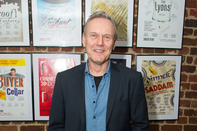 A photo showing a man smiling in front of a series of stage posters 