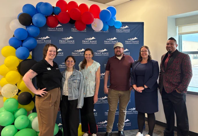 Six professionals stand in front of a Front Range Community College branded backdrop with a colorful balloon arch.