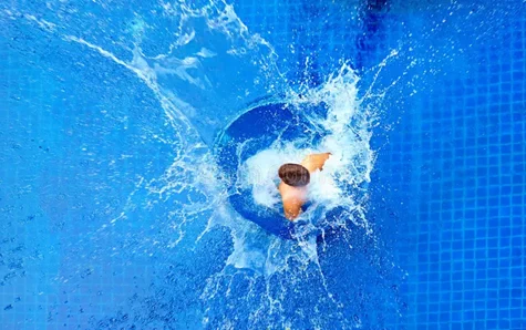 Top-down view of a person diving into a blue tiled pool, creating a large splash around them.