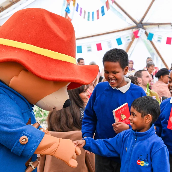 Paddington costume character shaking hands with two smiling school children, holding Paddington books