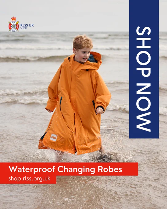 A person wearing an orange waterproof changing robe is walking along the shore with waves in the background. Text reads "Shop Now" and "Waterproof Changing Robes, shop.rlss.org.uk" with the RLSS UK Shop logo.