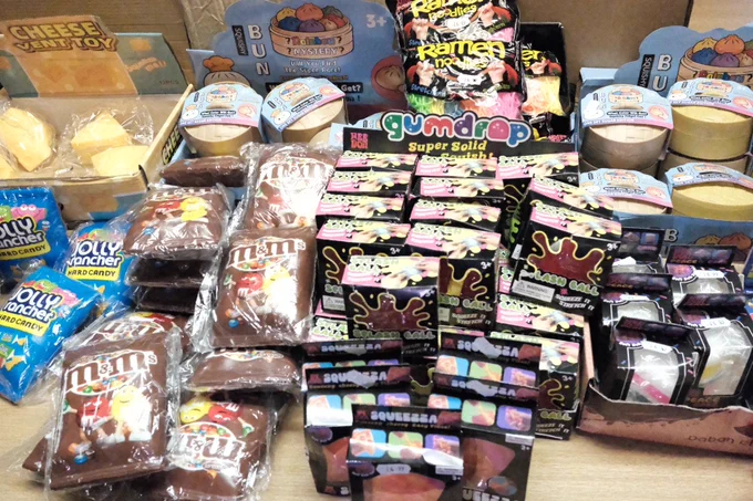 A display of seized squishy toys and candy, including M&M's, Jolly Ranchers, and various character-themed items.