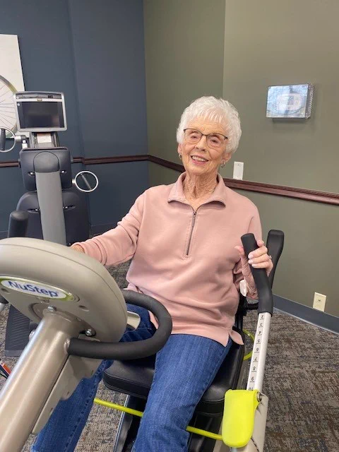 Elderly woman using a NuStep T4r recumbent cross trainer in a fitness wellness room at a senior living facility