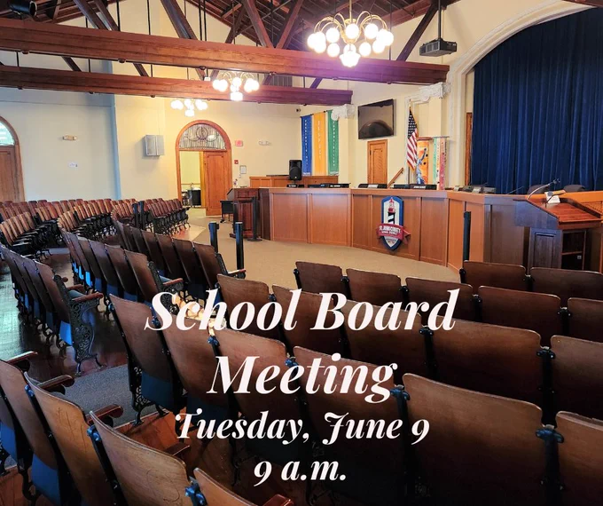 Empty school board meeting room with wooden chairs and a podium under chandeliers and exposed beams.