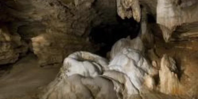 Stalactites and stalagmites inside a dimly lit limestone cave chamber with rough textured walls.