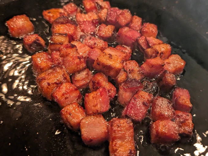 Large bacon chunks frying in a skillet