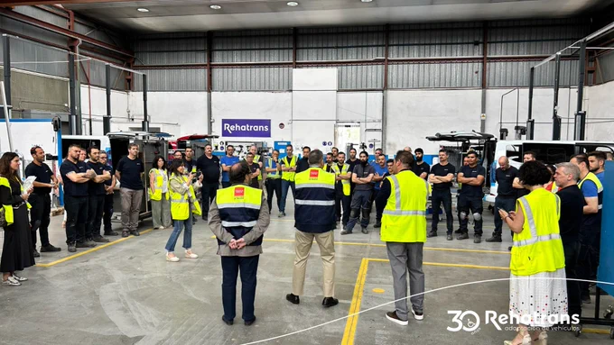 Equipo de Rehatrans reunido en un taller industrial, varios con chalecos reflectantes formando una ronda.