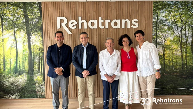 Cinco personas sonriendo frente a un panel de madera con el logotipo "Rehatrans" y un mural de bosque detrás.