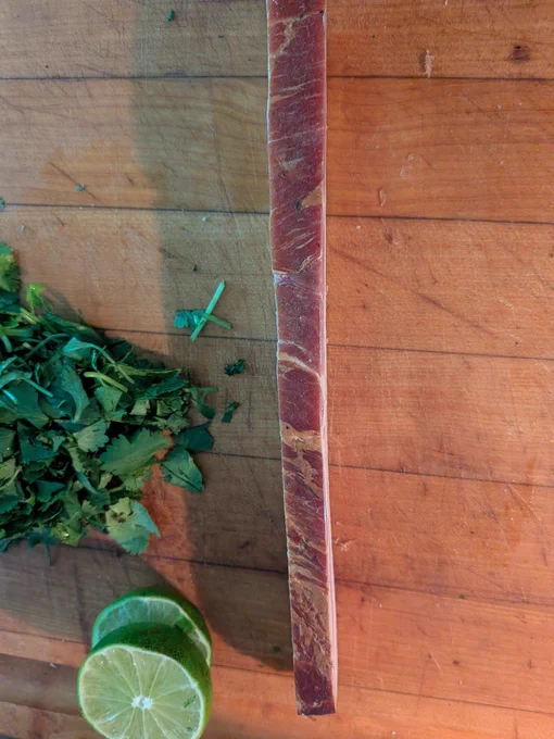 1/2" thick slice of bacon next to  lime slices and chopped cilantro