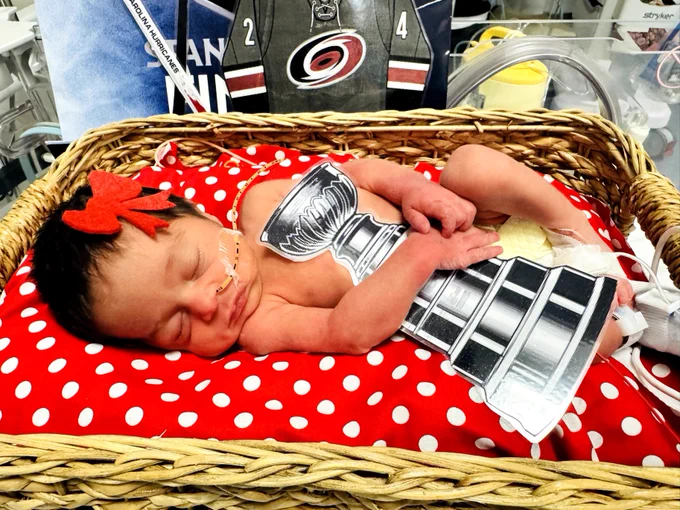 Several UNC Health Rex NICU babies wear Carolina Hurricanes-themed outfits while resting in their bassinets. Cutouts of Stormy, the Hurricanes mascot, and the Stanley Cup are displayed beside them as they celebrate the team's win.