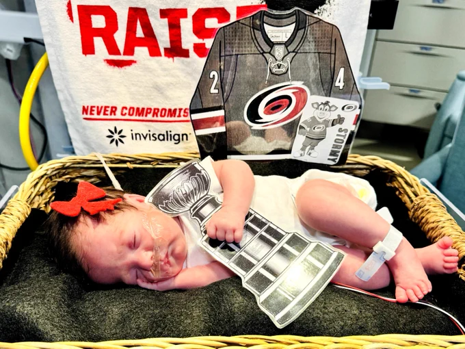 Several UNC Health Rex NICU babies wear Carolina Hurricanes-themed outfits while resting in their bassinets. Cutouts of Stormy, the Hurricanes mascot, and the Stanley Cup are displayed beside them as they celebrate the team's win.