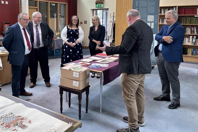 A group of people in Cardinal Tomás Ó Fiaich Library & Archive looking at historic documents. The group includes Maolíosa McHugh MLA, Pam Cameron MLA, Sian Mulholland MLA and Colm Gildernew MLA, Chair of the Committee for Communities.