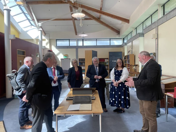 A group of people in Cardinal Tomás Ó Fiaich Library & Archive looking at historic artefacts. The group includes Maolíosa McHugh MLA, Pam Cameron MLA, Sian Mulholland MLA and Colm Gildernew MLA, Chair of the Committee for Communities.