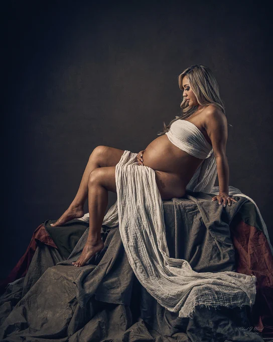Pregnancy Photography Phoenix: Pregnant woman sitting on a box with hands on her belly.
