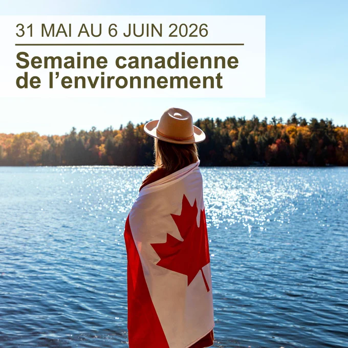Une femme avec un chapeau qui s’enveloppe dans un drapeau du Canada, debout au bord d’une rivière avec un ciel bleu et des arbres de l’autre côté de la rivière; le texte superposé en haut à gauche indique « 31 mai au 6 juin 2026, Semaine canadienne de l’environnement »