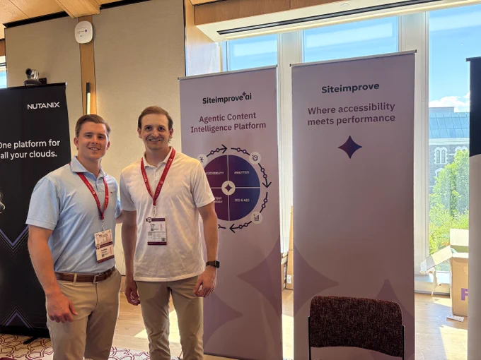 Two Siteimprove team members smile at the company's event booth. The booth features a branded maroon tablecloth, product demo monitors, and roll-up banners reading "Siteimprove.ai — Agentic Content Intelligence Platform" and "Siteimprove: Where accessibility meets performance."