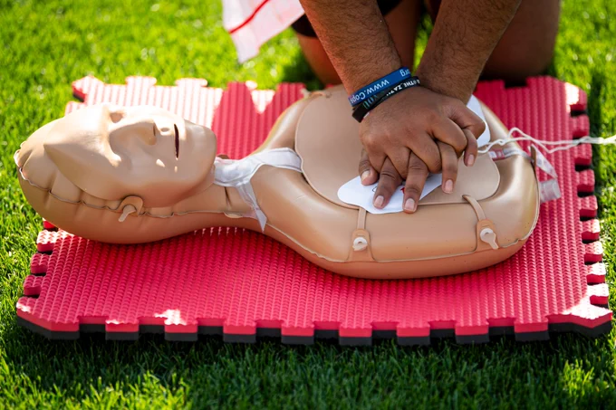 A participant in the hands-only CPR clinic performs CPR on a training manikin in the outfield grass.