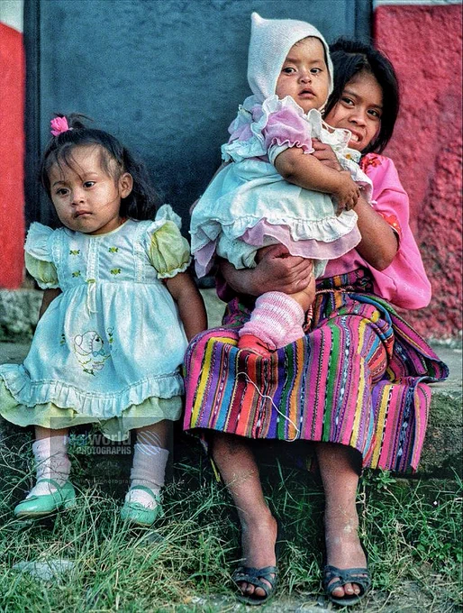 A family sit in a doorway in Guatemala City, Guatemala, Central America. 1992. Gary Moore photo. Real World Photographs. #photojournalism #Grok #streetphotography #X #Guatemala #nineties #vintage #travel #realworldphotographs #Nikon #Google #Copenhagen #garymoorephotography