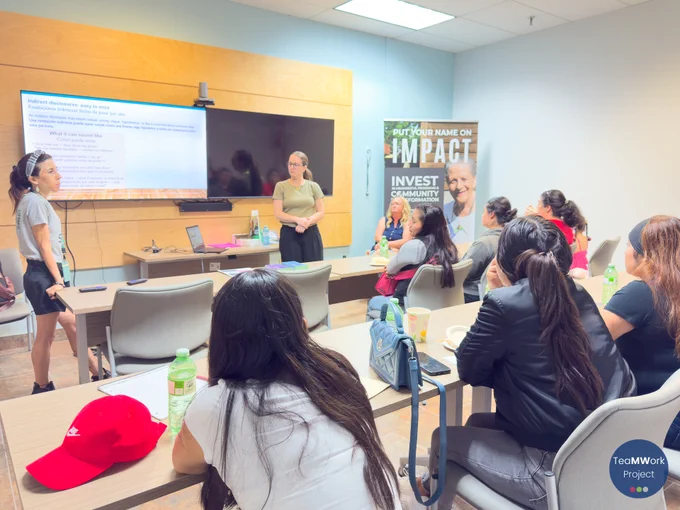 Presenter speaks beside a screen showing information on recognizing abuse, while attendees sit at tables with notes and refreshments, listening during an educational session at SECC.